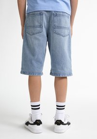 Shorts en denim bleu clair avec un ourlet retroussé, dotés de deux poches arrière, portés avec des chaussettes rayées blanches et noires et des baskets.