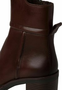 Bottine en cuir marron avec une forme arrondie, une couture piquée et une boucle à l'arrière. Présente un talon texturé avec des rayures horizontales.