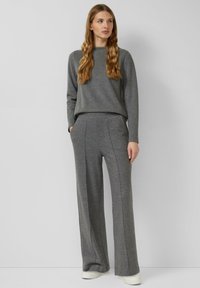 Szary sweter i spodnie o szerokich nogawkach wykonane z miękkiej tkaniny; sweter ma okrągły dekolt, a spodnie posiadają boczne kieszenie z przeszywanymi detalami.