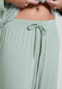 Lichtgroene loungekleding met een koord in de taille, gemaakt van zacht materiaal en met een ontspannen pasvorm. Het ontwerp bevat zachte plooien voor extra comfort.