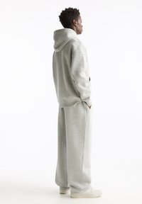 Grauer Kapuzenpullover und Sweatpants aus weichem Stoff, mit lockerer Passform und Taschen. Das Outfit wird mit hellen Sneakers abgerundet.