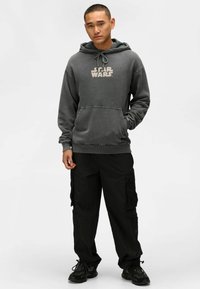 Grå huvtröja med "STAR WARS"-logga, texturerad tyg, kängurufickor, kombinerat med svarta cargobyxor och mörka sneakers.