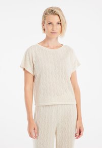 Top lavorato a maglia beige con motivo a diamante, maniche corte e colletto a girocollo. Il materiale sembra leggero e texture.