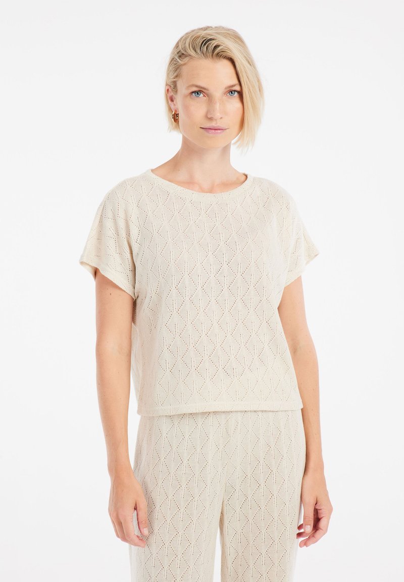 Top lavorato a maglia beige con motivo a diamante, maniche corte e colletto a girocollo. Il materiale sembra leggero e texture.