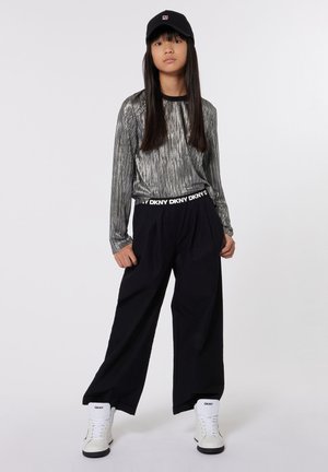 Zilveren lange mouw top met verticale strepen, zwarte wijde broek, zwarte pet en witte hoge sneakers met zwarte zolen en logo.