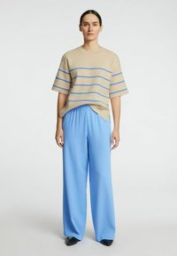 Maglia beige a maglia con strisce orizzontali blu, abbinata a pantaloni larghi azzurri chiari. Tessuto morbido, vestibilità rilassata e design semplice.