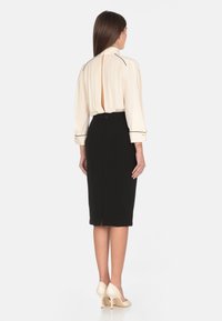 Blusa crema con collo alto e spacco sul retro, abbinata a una gonna a matita nera e scarpe con tacco beige. Design pulito e strutturato.