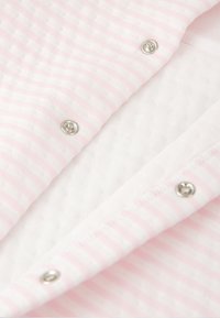 Detalle de tela abotonada que presenta un material ligero blanco con rayas rosas, broches plateados y un patrón texturizado.