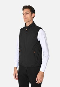 Gilet nero senza maniche in tessuto leggero, caratterizzato da un alto colletto, chiusura con zip e due tasche laterali con zip arancioni.
