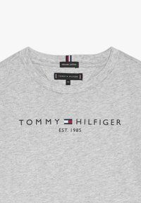 Szara koszulka z organicznej bawełny z okrągłym dekoltem, z logo "TOMMY HILFIGER" oraz napisem "EST. 1985" w kolorze czarnym. Metka zawiera szczegóły dotyczące rozmiaru i materiału.