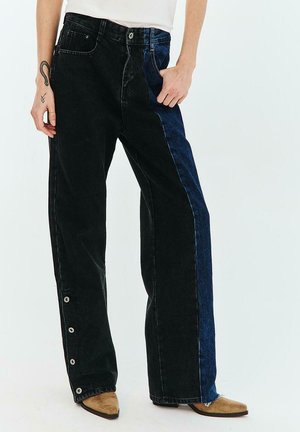 Dwukolorowe czarno-granatowe szerokie dżinsy z zatrzaskami wzdłuż zewnętrznego szwu, noszone z jasnobrązowymi spiczastymi butami.