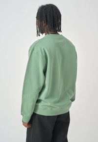 Green sweatshirt with long sleeves and a crew neckline, made of soft cotton material. Features ribbed cuffs and hem.