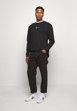 Black long-sleeve shirt with white embroidered logo, paired with dark pants and white sneakers featuring a black star logo. Simple design, relaxed fit.