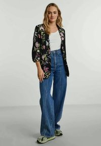 Fekete virágmintás blézer, fehér ing, magas derekú kék trapézfarmerek, zöld tornacipők. A blézer rózsaszín és zöld virágmintákra van díszítve.