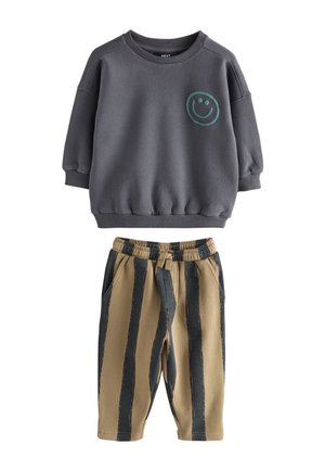 Dunkelgraues Sweatshirt mit langen Ärmeln, türkisfarbenem Smiley-Gesicht und beigen Hosen mit breiten schwarzen vertikalen Streifen, elastischem Bund und Seitentaschen.
