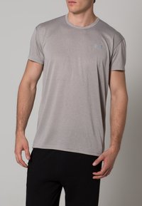 Grå kortärmad t-shirt i mjukt material, med rund halsringning och en liten, diskret logo i ljusblått på bröstet.