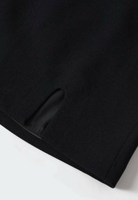 Tessuto nero con una superficie liscia presenta un dettaglio a spacco all'orlo. Il design è semplice e contemporaneo, focalizzato su linee pulite.
