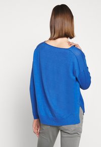 Blauer leichter Pullover mit lockerer Passform, weitem Ausschnitt und geripptem Saum. Der Stoff sieht weich aus und hat seitliche Schlitze für Bewegungsfreiheit.