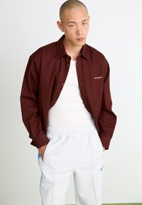 Maroon button-up shirt with a collar, white undershirt, and light gray sweatpants featuring blue side stripes and zippered pockets.