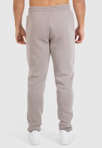 Lichtgrijze sweatpants van zachte stof met een elastische tailleband. Voorzien van taps toelopende benen en zijzakken, gecombineerd met witte sneakers.