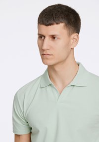 Ljusgrön polo t-shirt med klassisk krage och korta ärmar, med en mjuk textur och en subtil v-ringad design.