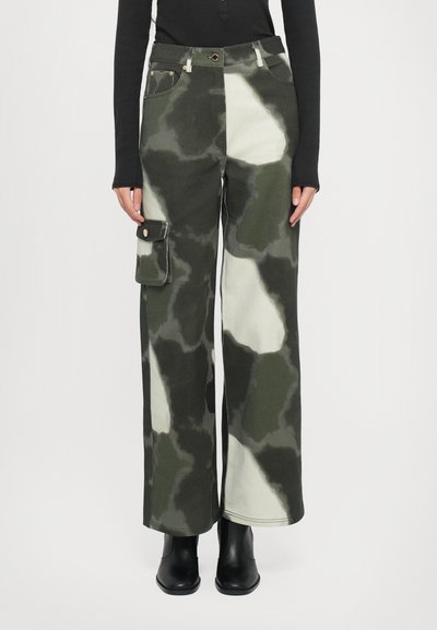 Pantalones cargo en un patrón de camuflaje verde y crema, hechos de una tela resistente, con bolsillos laterales y un diseño de corte holgado.