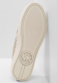 Semelle de chaussure de sport beige avec un motif antidérapant texturé. Présente un logo circulaire en relief et des bords lisses. Conçue pour un usage décontracté.