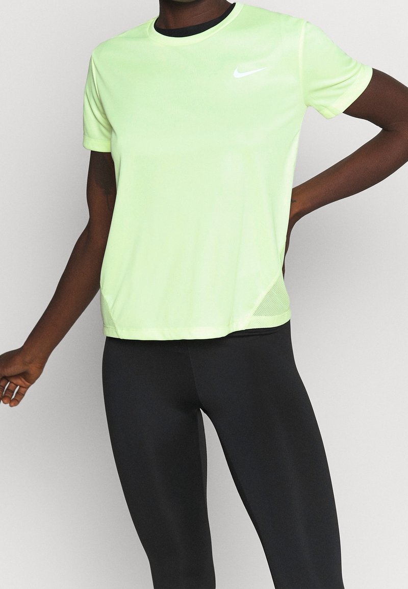 Osoba w jasnozielonej koszulce Nike z krótkim rękawem i czarnych legginsach, stojąca z jedną ręką na biodrze, a drugą swobodnie opuszczoną.