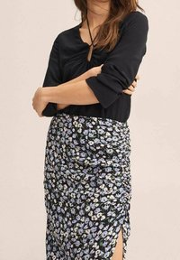 Musta pusero, jossa on kerätty kaula-aukko ja kolmannen neljänneksen hihat, yhdistettynä kukkakuosisesti hamppariin, jossa on rypytystä ja halkio.