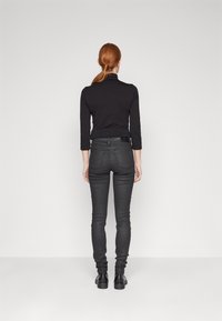 Top negro de manga larga y jeans ajustados gris oscuro combinados. El material parece suave, con un diseño ajustado y un estilo minimalista.