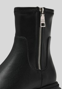 Stivale alla caviglia in pelle nera con lampo argento visibile e incisione "Steve Madden" sul gancio della lampo, cuciture dettagliate sulla parte superiore.