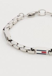 Ασημένιο μεταλλικό βραχιόλι με αλυσίδα και ορθογώνιο κούμπωμα που διαθέτει μικρό λευκό, κόκκινο και μπλε ριγέ σχέδιο σε λευκό φόντο.