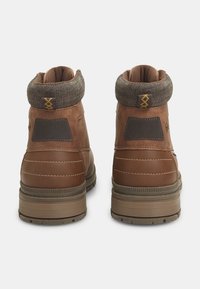 Botas de tobillo de cuero marrón con un cuello texturizado en verde oscuro, costuras en contraste y suelas de goma con un patrón en la suela.