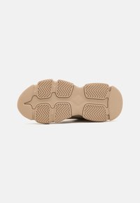 Semelle d’une chaussure beige avec une bande de roulement en caoutchouc segmentée avec des motifs en zigzag pour l’adhérence et des rainures flexibles pour le mouvement.
