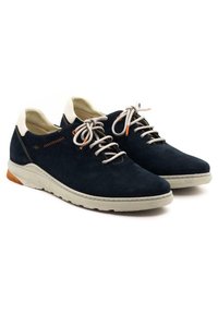 Zapatos de ante azul marino con una superficie texturizada, detalles en blanco y cordones beige. Cuentan con una suela acolchada con un detalle naranja en el talón.