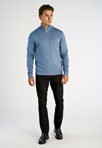 Blauwe trui met ritssluiting van gestructureerde gebreide stof, gecombineerd met zwarte slim-fit broek en gepolijste zwarte schoenen.