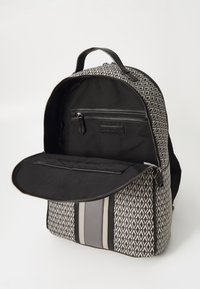 Ruksak s uzorkom sivoj vanjštini, gornjom ručkom i crnim zatvaračem; sadrži unutarnje džepove i prugasti detalj s prednje strane.