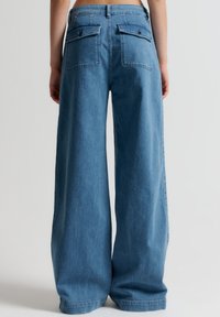 Vida jeans med vida ben i ljusblått. Har bakfickor med knappdekorationer, hög midja och en avslappnad passform. Slät, mjuk textur.