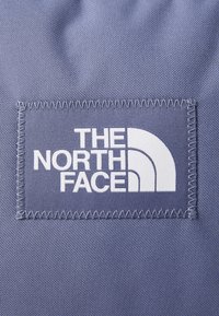 Modrý látkový nášivka s bielym embosovaným textom "THE NORTH FACE" a výrazným polkruhovým logom. Šité okraje. Hladký povrch.