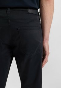 Svarta byxor med en mjuk yta, bakfickor och en märkesläderlapp. Designen är skräddarsydd och modern.