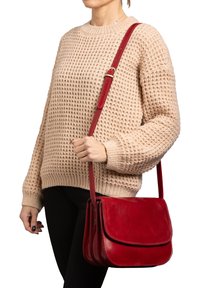 Borsa a tracolla in pelle rossa con chiusura a pattina e tracolla regolabile. Presenta una superficie liscia e dettagli di cucitura.