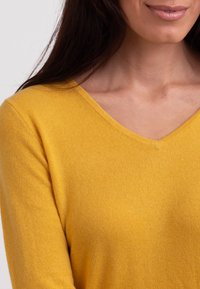 Gul stickad tröja med v-ringning, med en mjuk textur och slim fit som framhäver kroppens form och det släta tyget.