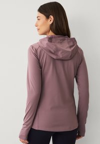Maglietta a maniche lunghe con cappuccio in mauve tenue realizzata in un tessuto liscio e elastico. Caratterizzata da una vestibilità comoda e cuciture rinforzate. Branding minimale vicino al collo.