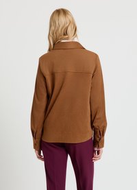 Chemise marron à manches longues en tissu doux, avec col, poignets boutonnés et un empiècement au dos, associée à un pantalon bordeaux.