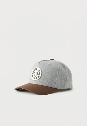 Gorra de béisbol de tela gris claro con una visera curvada marrón y un parche blanco redondo con la inscripción "Brixton MFG. CO." en el frente.