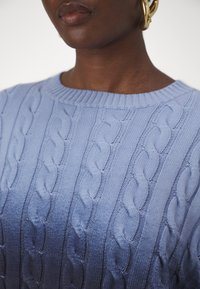 Ljusblå stickad tröja med ett texturerat kabelmönster och en ribbad rund halsringning. Mjuk, elastisk tyg med en slät yta.