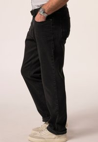 Jeans de mezclilla negros con un corte relajado, diseño de cinco bolsillos, detalles de costura visibles y una textura ligeramente deslavada. Combinados con zapatillas blancas.