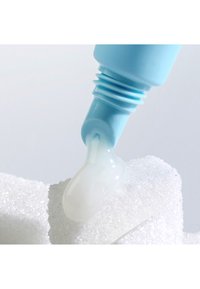 Tubo spremibile con un cappuccio azzurro chiaro che eroga un gel lucido e traslucido su una superficie bianca testurizzata.