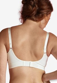 Valkoinen, saumatonta rintaliiviä säädettävillä olkaimilla ja hakasilmällä. Sujuva kangas, U-muotoinen selkäosa, minimalistinen tyyli.