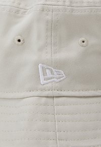 Cremefarvet bomulds cap med lodret ribbet tekstur. Har et broderet logo i hvid, to luftventiler og en buet skygge.